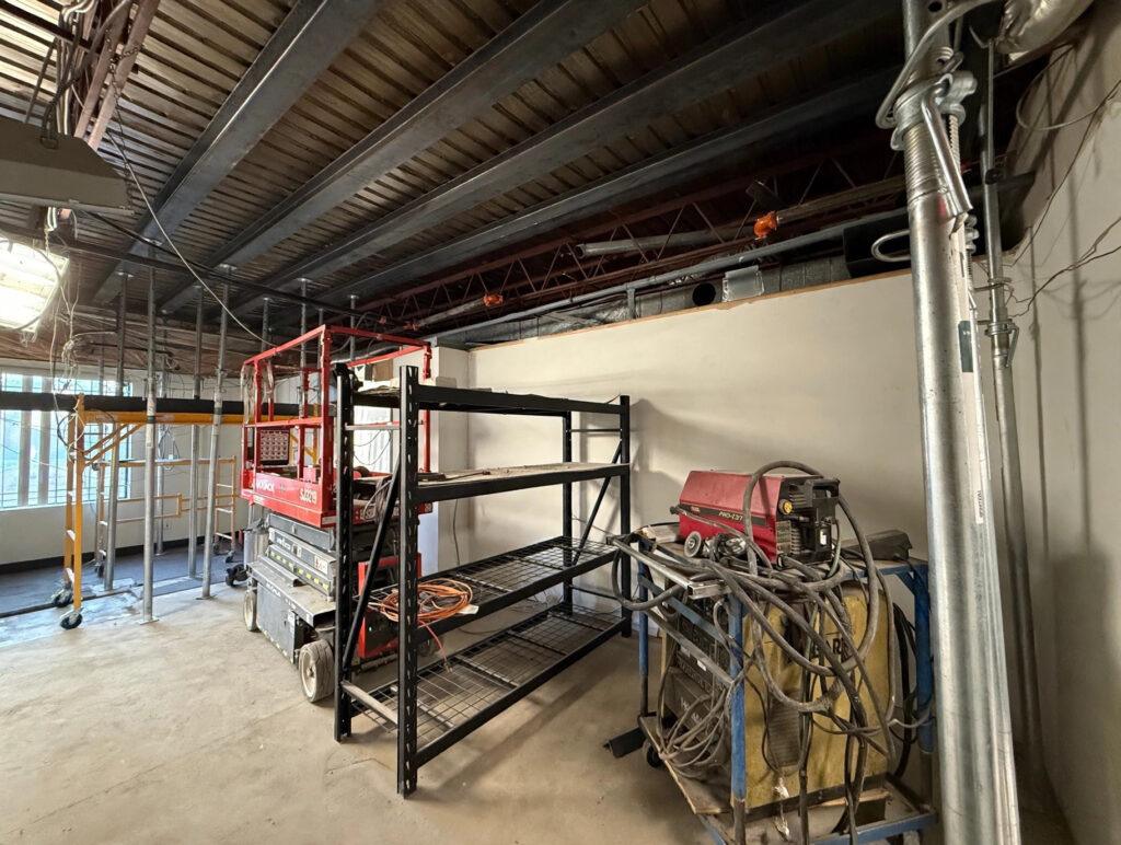 Commercial interior with steel ceiling beams, scissor lift, and shoring during structural work