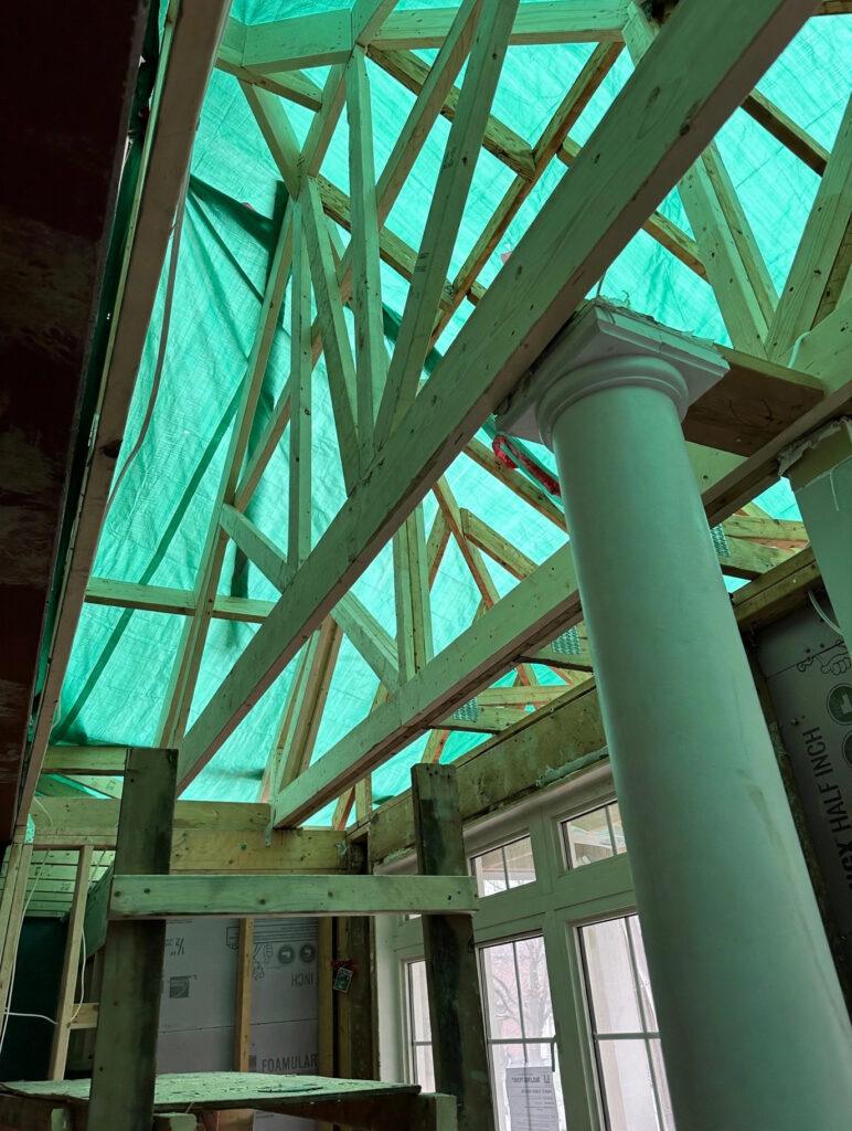 Wooden roof trusses and structural framing under a protective tarp during a residential addition